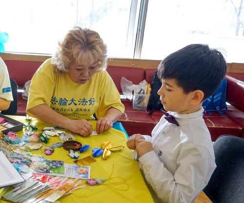 A Falun Dafa practitioner shows a boy how to fold origami lotus flower at the event held at Moskvich Cultural Center in Moscow.