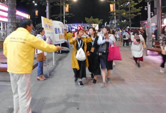 2 Falun Dafa practitioners offering a flyer to visitors.