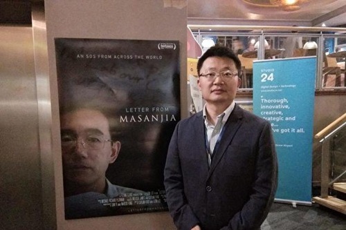 Leon Lee, director of Letter from Masanjia , stands next to a poster for the documentary during the Cambridge Film Festival.