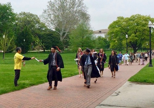 906aa2b9513dcdc2dbb8d4f669cb16b7 A practitioner passes out flyers and lotus flowers to graduates and their families in front of the OSU library.