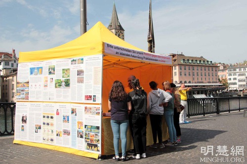 A practitioner tells people about the persecution while others demonstrate the Falun Dafa exercises.