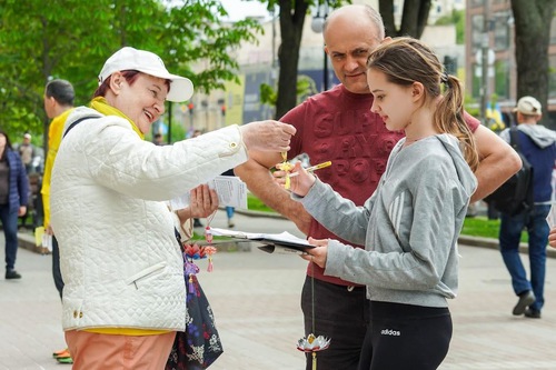 A practitioner (left) explains what Falun Gong is and hands a girl a lotus flower.