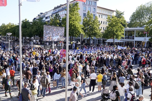 People watch two large screens as practitioners enter City Hall Square.